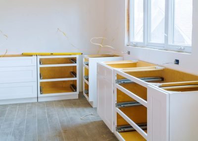 A kitchen under renovation with white cabinets installed and empty spaces for granite countertops and appliances.