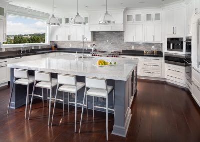 Modern kitchen with white cabinetry, a marble island, stainless steel appliances, pendant lighting, and dark wood flooring. The sleek kitchen cabinets provide ample storage space while maintaining an elegant look.
