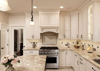 Elegant kitchen with white cabinets, granite countertops, a stainless steel stove, and decorative lighting.