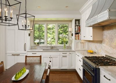 Spacious kitchen with white cabinets, granite countertops, a large window, wooden dining table with green pears, and modern light fixtures. The elegant flooring ties the room together perfectly.