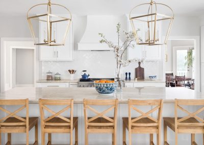 A bright kitchen with a marble island, wooden chairs, hanging gold lights, and a vase with branches as the perfect finishing touch.