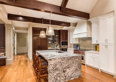 Modern kitchen with wooden floors, an island featuring quartz countertops, hanging lights, and dark wood beam ceiling accents.