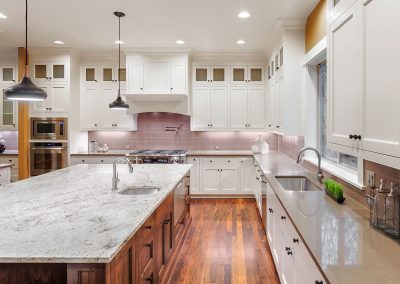 Modern kitchen with a large island, white cabinetry, stainless steel appliances, and hardwood flooring. The sleek quartz countertops add a touch of elegance to the space.