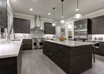 Modern kitchen with dark wood cabinets, stainless steel appliances, large island with a quartz countertop, and pendant lighting.
