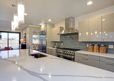 Modern kitchen with a white marble island, stainless steel appliances, grey kitchen cabinets, and a backsplash made of glazed tiles.
