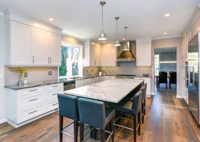 Modern kitchen with white cabinets, stainless steel appliances, a marble island countertop alongside granite kitchen countertops, and dark wooden bar stools.