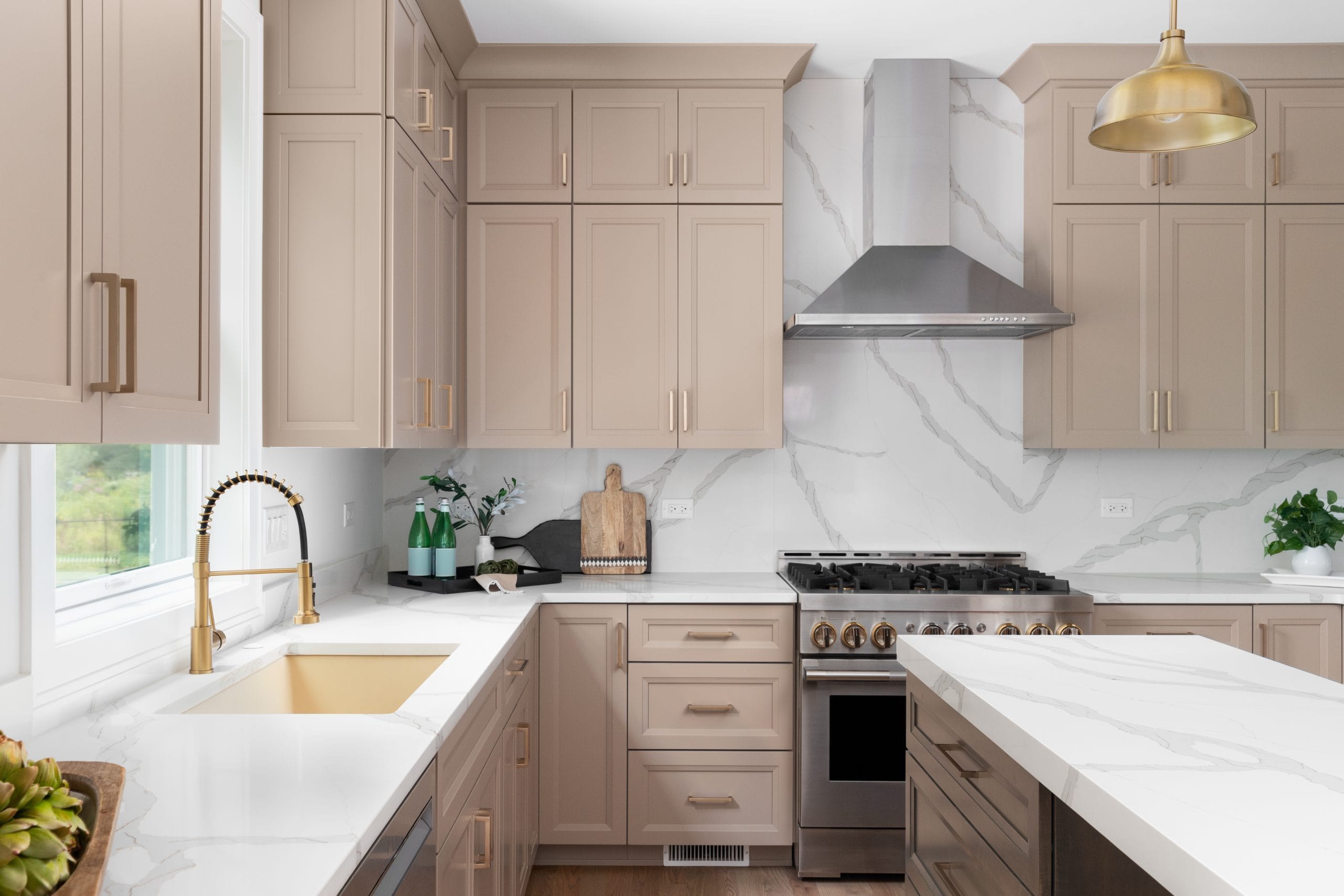 A kitchen detail with brown cabinets, marble countertop and backsplash, wood island, and gold faucet, sink, and light fixtures. No brands or labels. The perfect stone