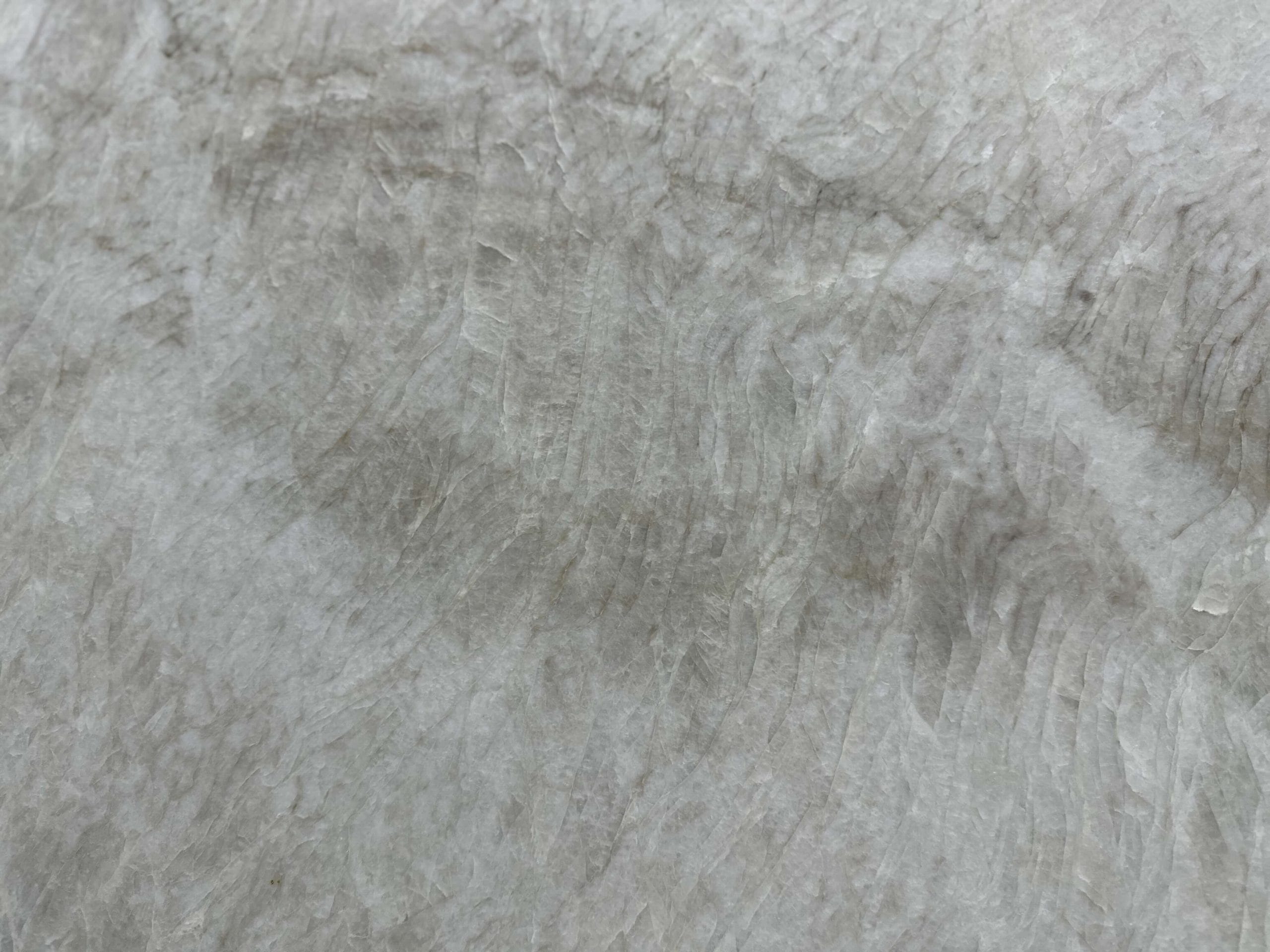 Close-up of a textured, pale gray stone surface with subtle wavy lines and layered patterns.