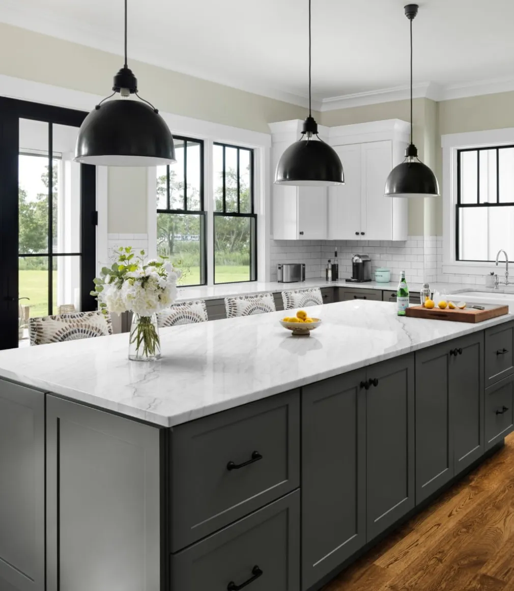 ivanti-areas-2 Modern kitchen with a marble island, gray cabinets, white upper cabinets, and black pendant lights.